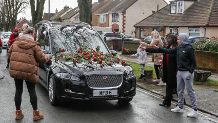 Members of the public place red roses on a hearse