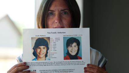 Jennifer Mogensen holds up a missing poster for her adopted sister Jonelle Matthews in 2019