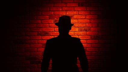 Silhouette of a man wearing a fedora on a red brick background