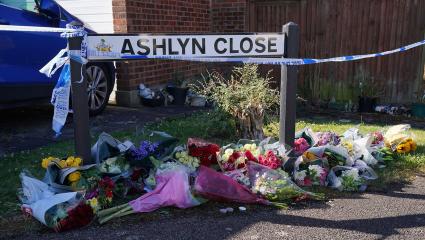 Floral tributes are left under a road sign for 'Ashlyn Close' that is also covered in police tape