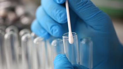 Forensic scientist wearing blue gloves puts a cotton swab inside a test tube