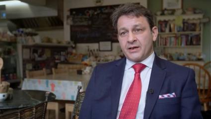 Local journalist Jez Hemming discussing the story of the Machete Killer in Wrexham. He is seen sitting in a cafe facing the camera and wearing a suit and tie