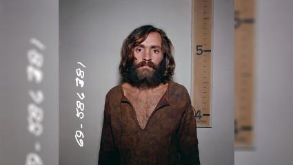 Charles Manson mugshot in front of a height chart that shows him to be a few inches taller than five foot