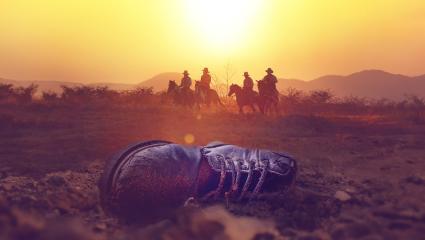 Men on horseback overlook a discarded boot in the Texas desert