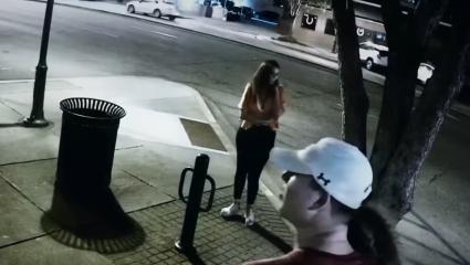 A CCTV screen grab showing Samantha Josephson on her phone outside a bar ordering an Uber. It is at night and she is stood alone, but other people are visible walking past her