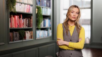 Laura Whitmore standing with her arms crossed in front of a large bookcase