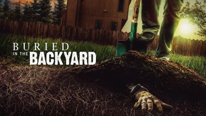 A hand appears the lawn in a backyard while a man stands with a shovel above it