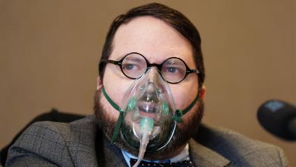 Nicholas Rossi (Alahverdian) speaking at a press conference while wearing an oxygen mask