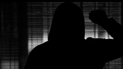 Silhouette of a man knocking on a glass door in the darkness
