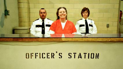 Aileen Wuornos smiling in an orange prison jumpsuit at the officer's station