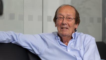 Fred Dinenage sitting with his arm up on a sofa wearing a blue shirt
