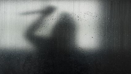 Silhouette of someone wielding a knife behind frosted glass