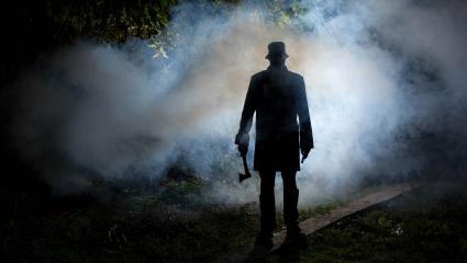 Silhouette of a man standing in a dark and smoky forest holding an axe