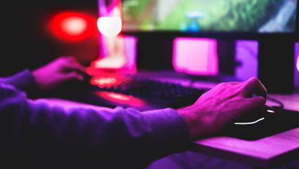 Someone using a PC set up to play an online game with purple lights shining on them