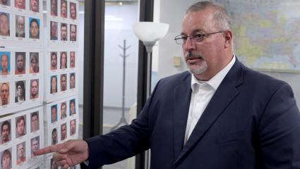 A detective points at a board full of mugshots