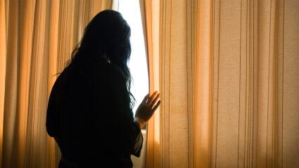 A woman cautiously looking out of her closed curtains
