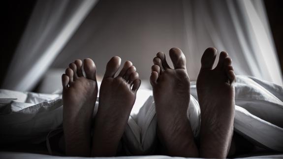 Two pairs of feet stick out the bottom of a duvet