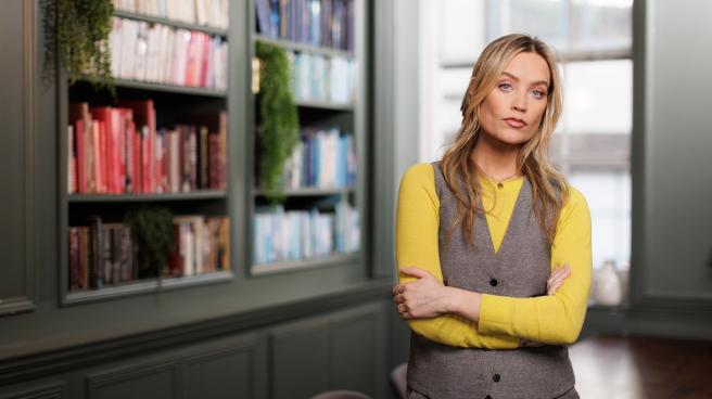 Laura Whitmore standing with her arms crossed in front of a large bookcase