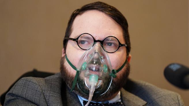 Nicholas Rossi (Alahverdian) speaking at a press conference while wearing an oxygen mask