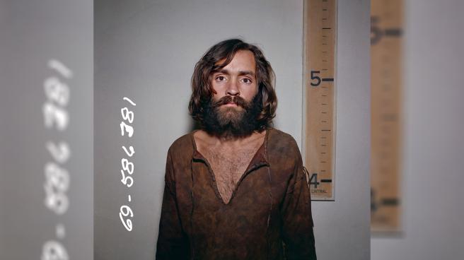 Charles Manson mugshot in front of a height chart that shows him to be a few inches taller than five foot
