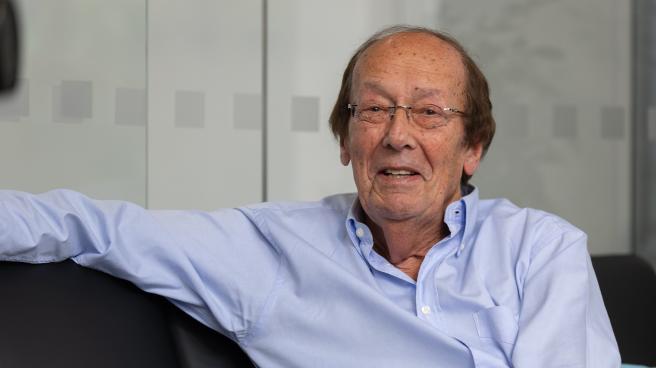 Fred Dinenage sitting with his arm up on a sofa wearing a blue shirt