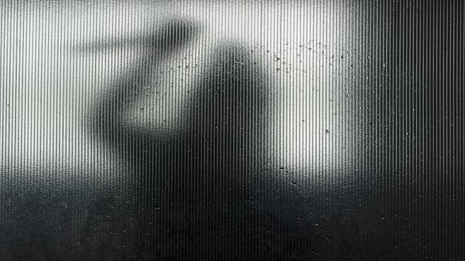 Silhouette of someone wielding a knife behind frosted glass