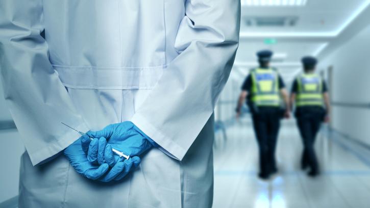 A stock image showing a person holding a syringe whilst police are in the distance