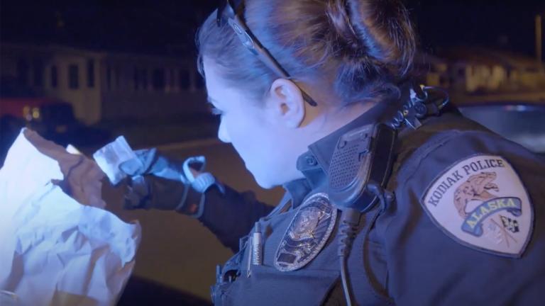 A female police officer holding up and inspecting a bag of meth