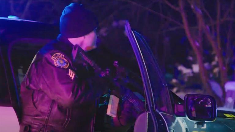 Policeman holds a gun next to his car at night time