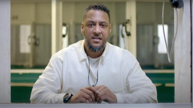 Kenneth Foster sitting behind a screen in a white prisoner uniform