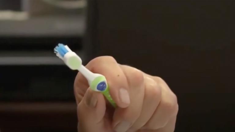 A green and blue toothbrush held in a man's hand