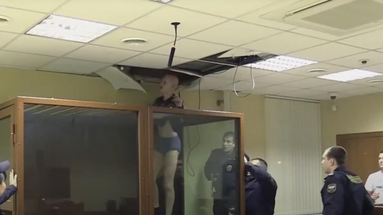 A prisoner tries to escape from his court box by going through the ceiling tiles