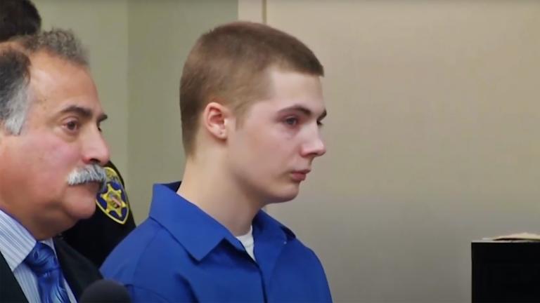 Dylan Schumaker wearing a blue prison jumpsuit in court