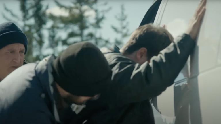 Police search a man with his hands up against the side of a van