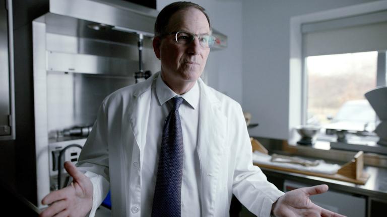 A man in a white lab coat gestures with his hands