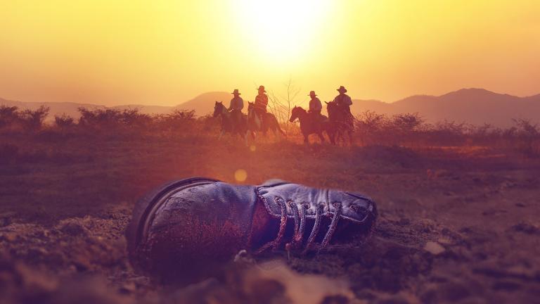 Men on horseback overlook a discarded boot in the Texas desert
