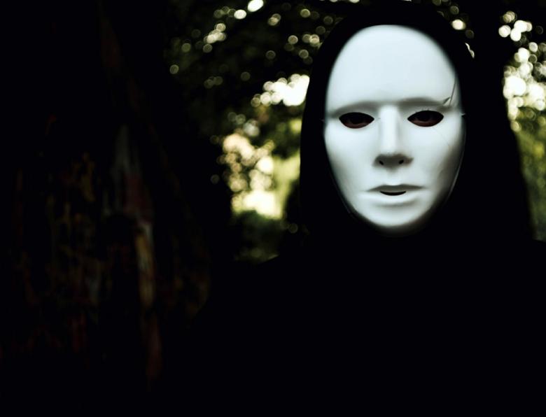 A hooded figure wearing a white mask