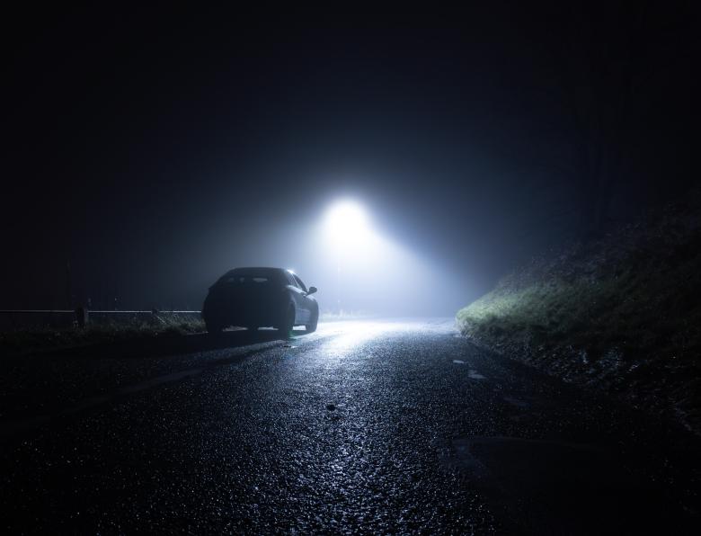 A lone car parked on the side of a rural road on a dark winter's night
