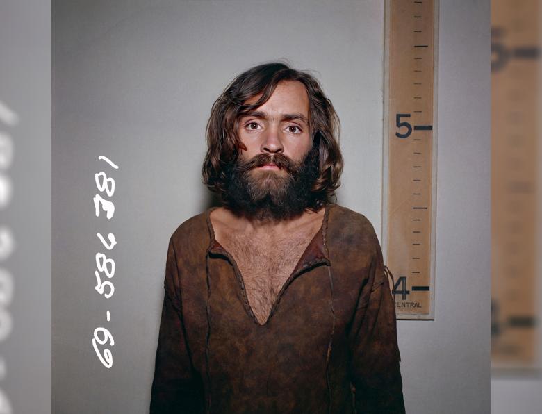Charles Manson mugshot in front of a height chart that shows him to be a few inches taller than five foot