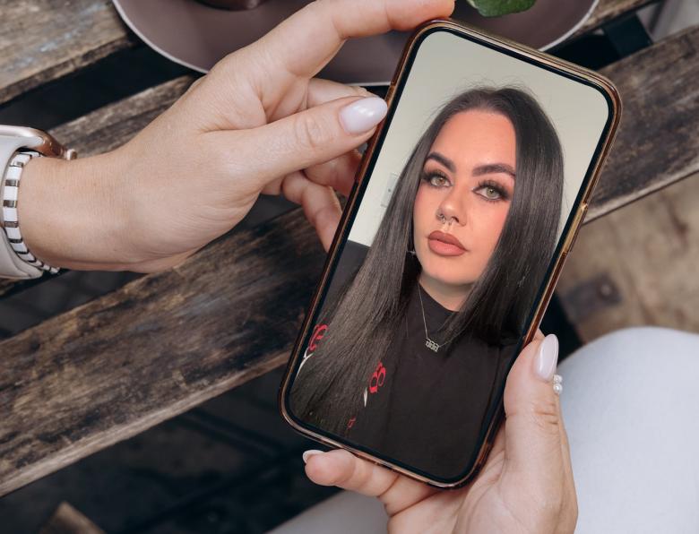 A woman holding a smartphone with an image of True Crime Caitlyn on