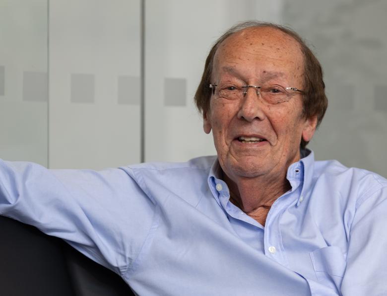 Fred Dinenage sitting with his arm up on a sofa wearing a blue shirt