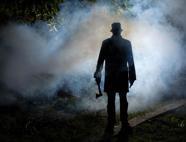 Silhouette of a man standing in a dark and smoky forest holding an axe
