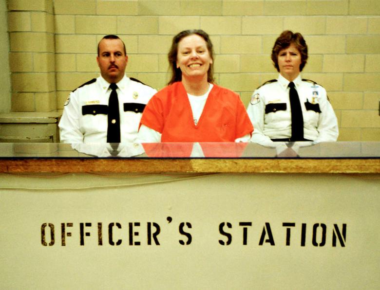 Aileen Wuornos smiling in an orange prison jumpsuit at the officer's station