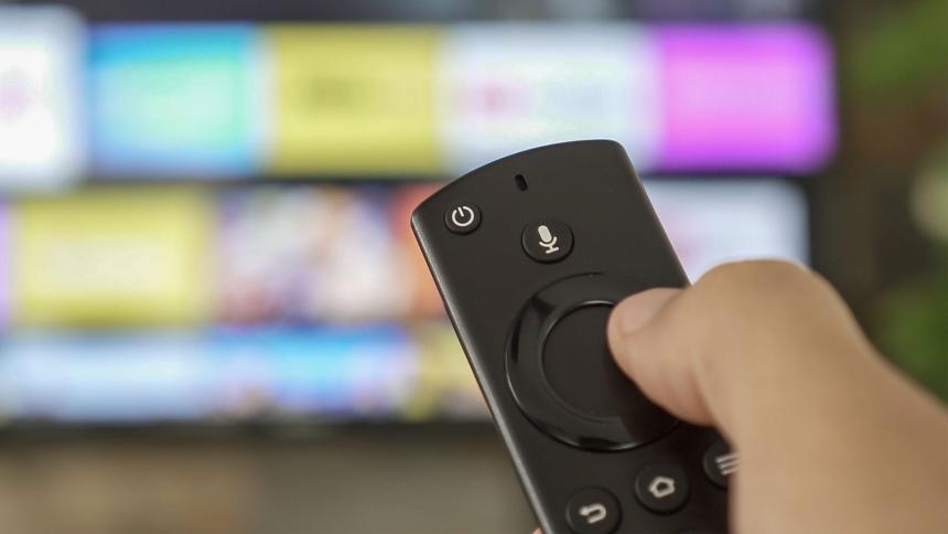 Male hand holding the TV remote control and changing TV channels
