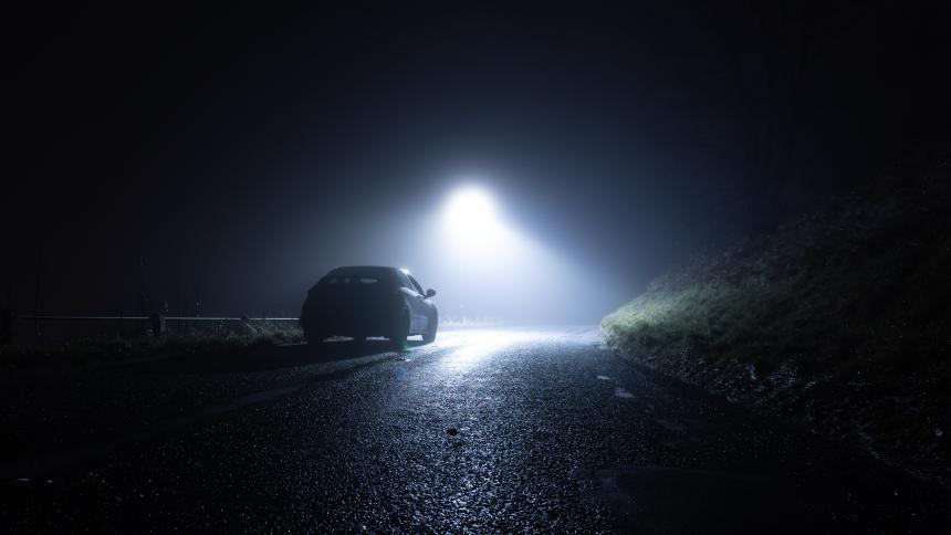 A lone car parked on the side of a rural road on a dark winter's night