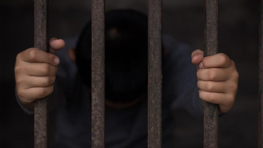 A child's hands holds onto prison bars from the inside