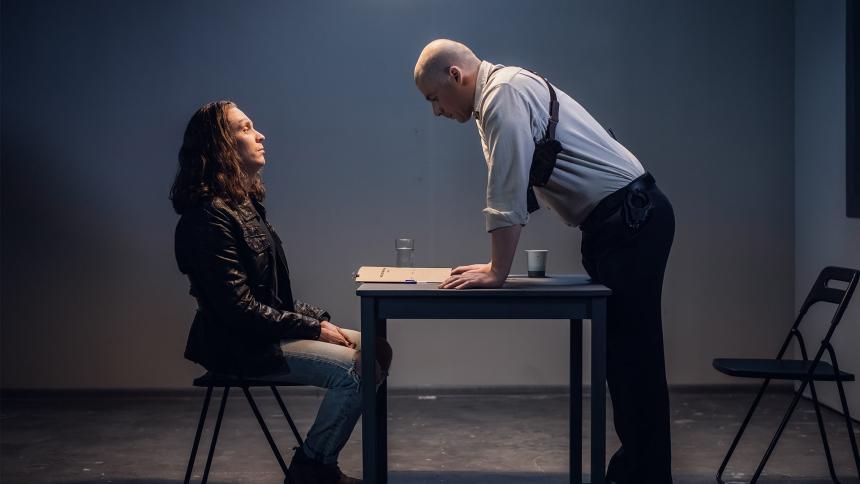 A policeman charges a man detained in handcuffs while inside an interrogation room.