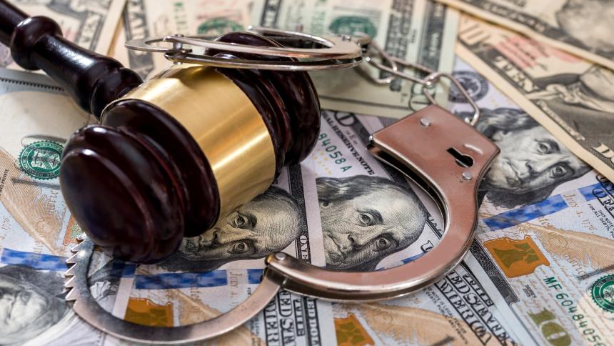 A stock photo of a courtroom gavel with police handcuffs and a background made of money banknotes