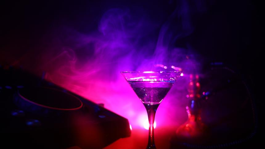 A photograph of a martini drink with an olive inside and disco lights behind