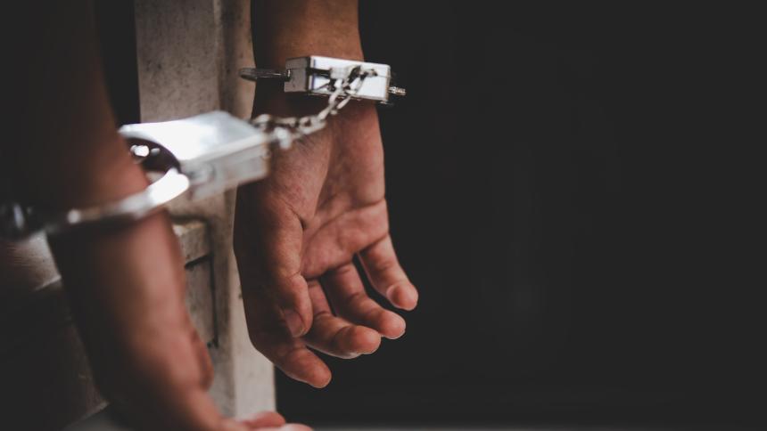 A photograph of a person handcuffed, behind jail bars